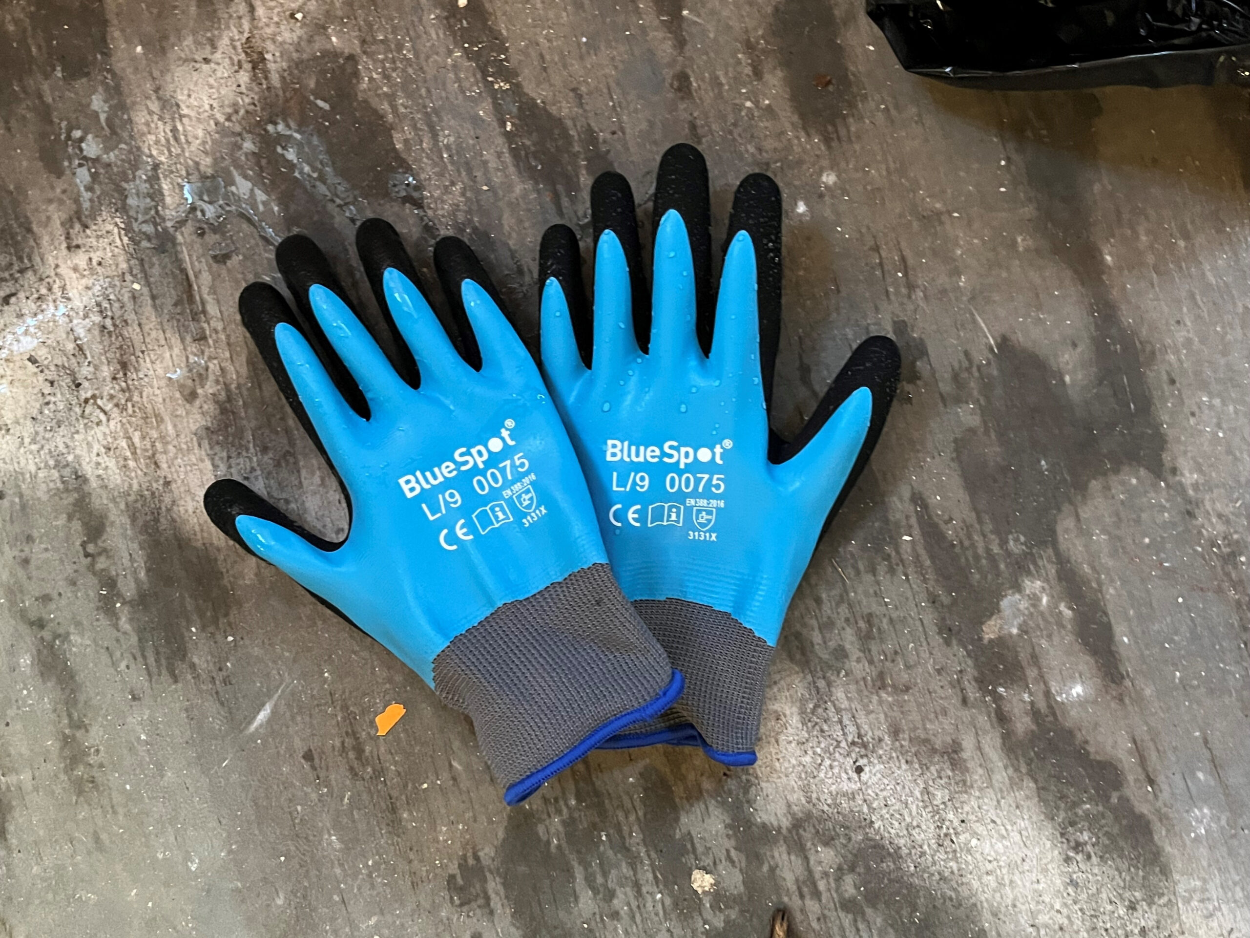 Pair of blue latex work gloves with black fingertips on a wet surface.