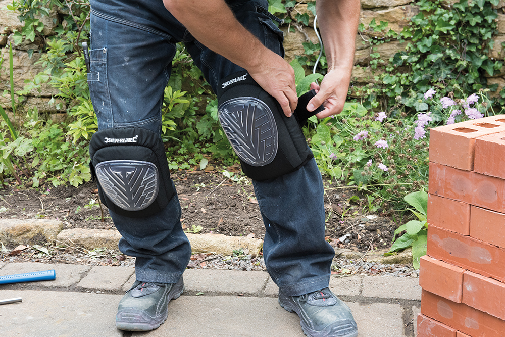 Person wearing Silverline Hard Cap Gel Knee Pads while working outdoors near a brick wall.