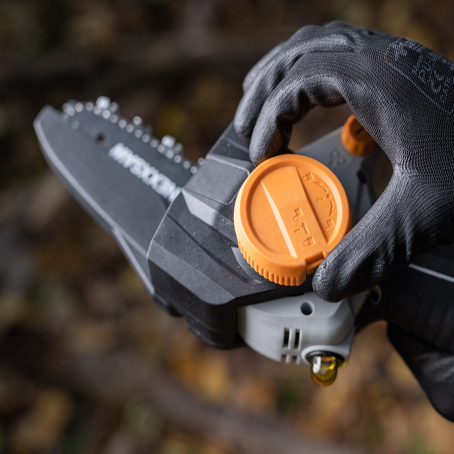 Close-up of a person adjusting the orange dial on a Batavia NEXXSAW 18V Cordless One-Handed Pruning Chainsaw.