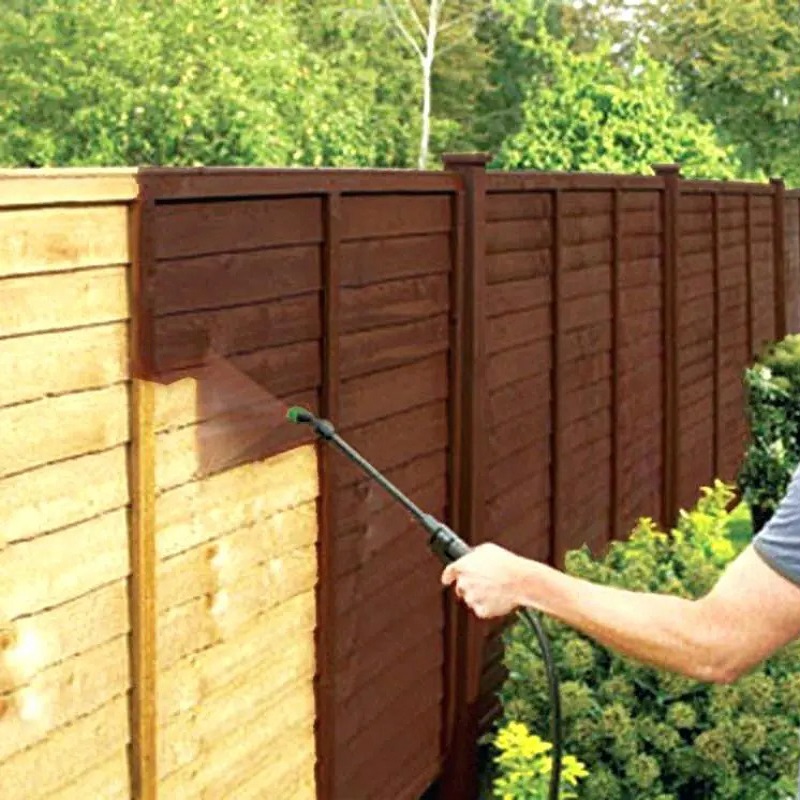 Person using a pressure sprayer on a wooden garden fence.