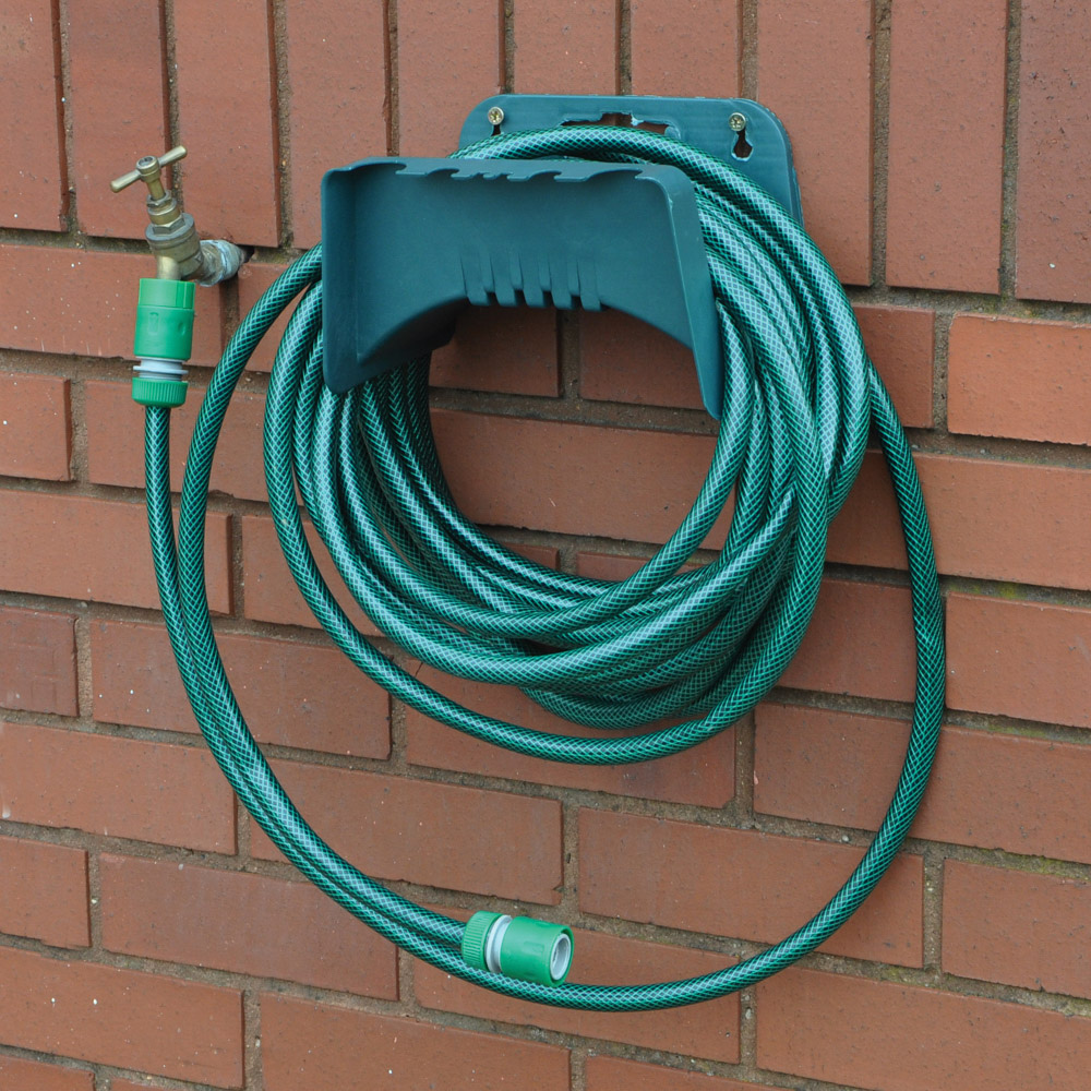 A green garden hose coiled on a wall-mounted hanger attached to a brick wall.