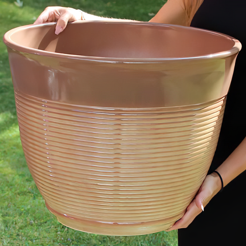 Person holding a large mottled ceramic flower pot in a garden setting.