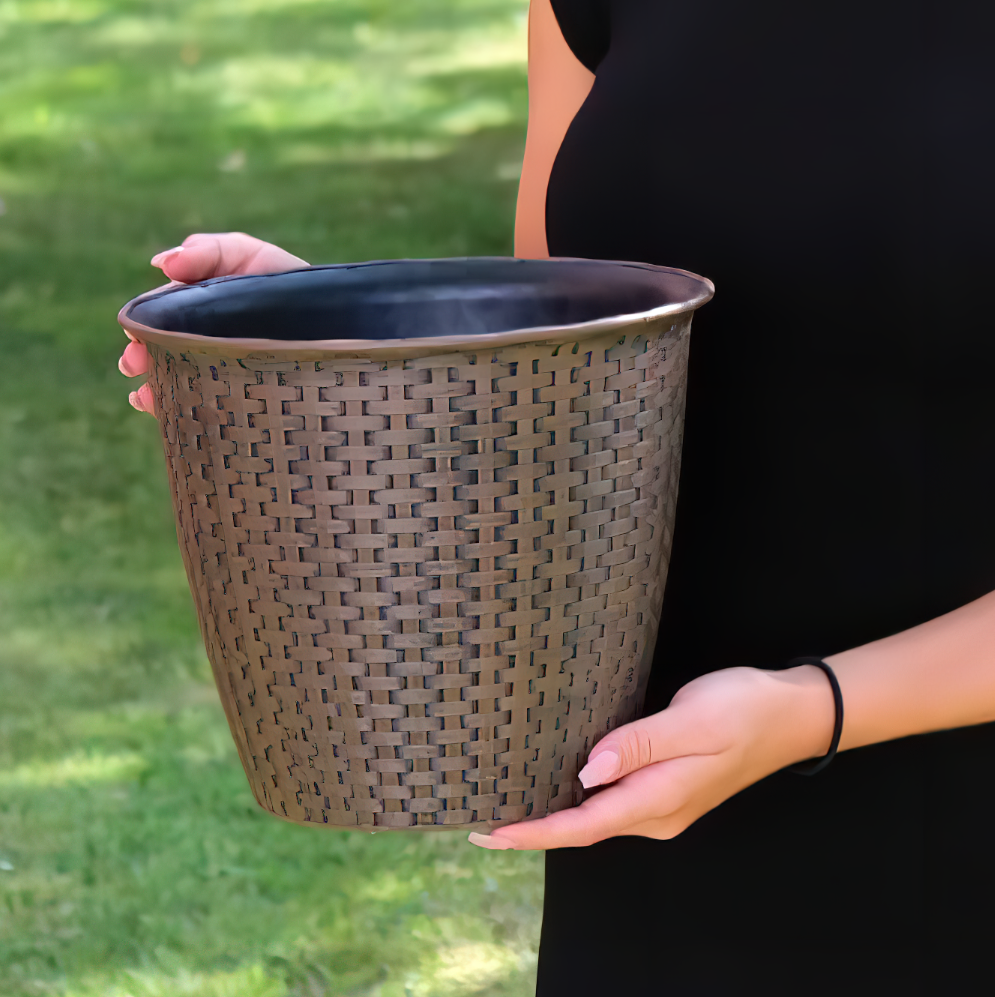 A person holding a 13.5 inch interwoven rattan garden flower pot against a grassy background.