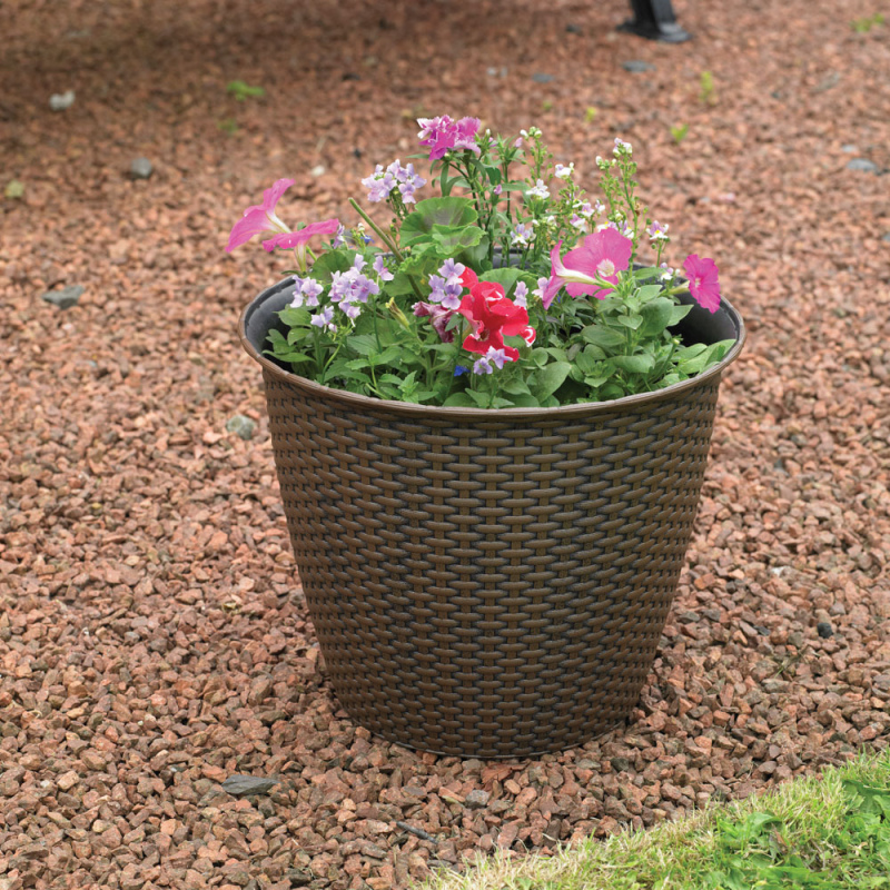 Interwoven rattan garden flower pot with colourful flowers on gravel.