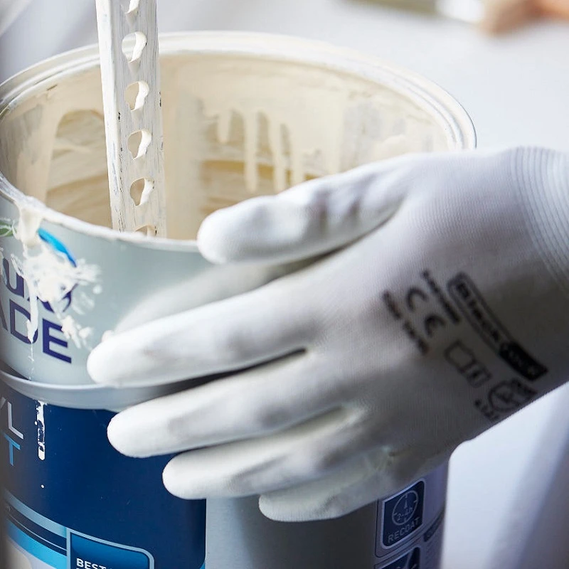 A close-up of a hand wearing BlackRock lightweight gripper work gloves, size 10, XL, holding a paint can.