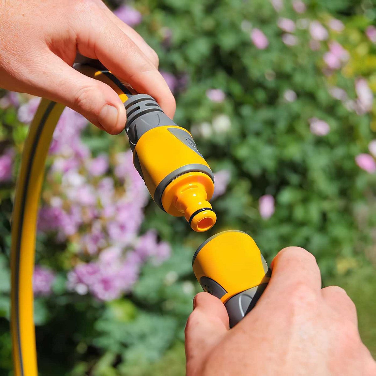 Hands connecting a yellow hose pipe with a double male hose pipe straight adapter joiner in a garden setting.