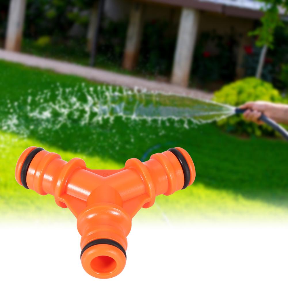 Orange 3-way hose pipe connector adapter on a blurred garden background.