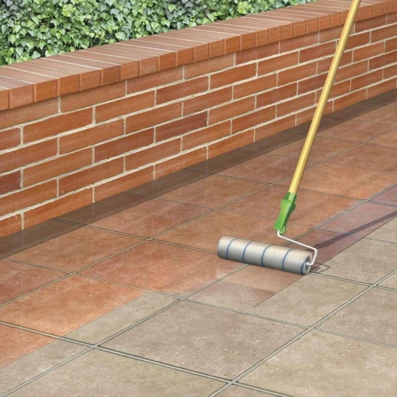 A roller applying clear coat sealer on block paving next to a brick wall.