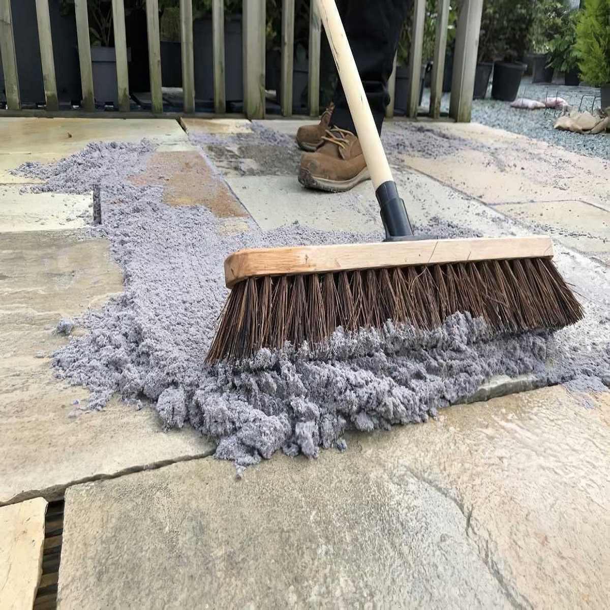 A person using a broom to spread Geo-Fix All Weather Jointing Compound in Slate Grey between stone paving slabs.