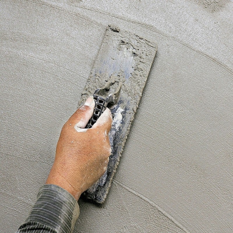 A hand using a trowel to smooth mortar on a wall surface.
