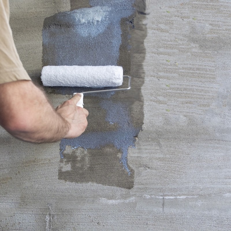 Person applying a waterproof bonding agent on a concrete wall with a paint roller.