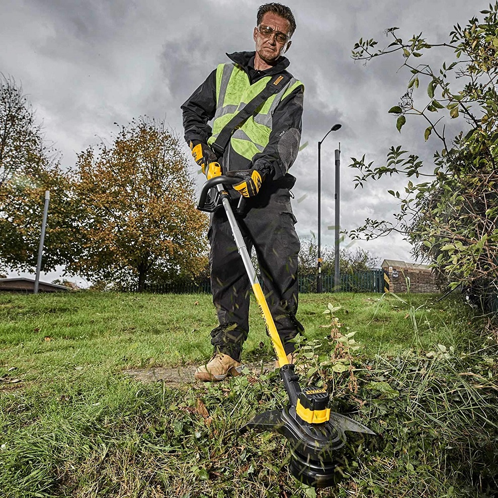 Person using a DeWalt cordless brushless 18v grass strimmer on a grassy area.