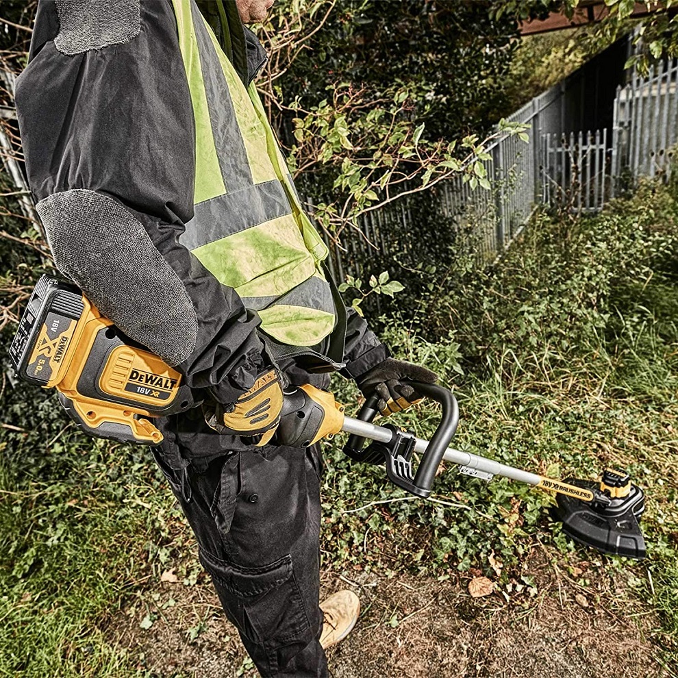 Person using a DeWalt cordless brushless 18v grass strimmer in a garden.