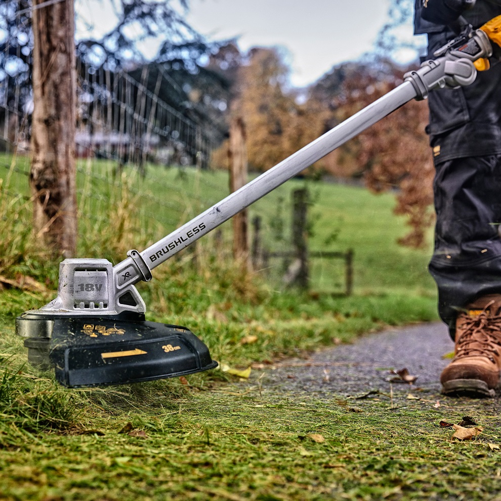 Person using a DeWalt cordless brushless folding grass strimmer on a grassy path.