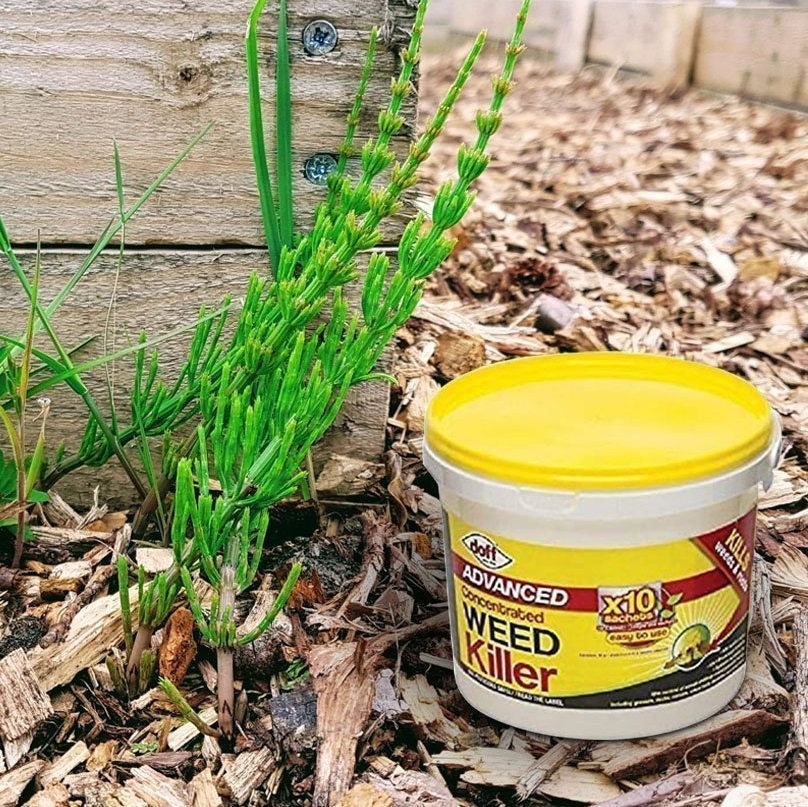 Container of Doff Advanced Weed and Root Killer placed on garden mulch next to green weeds.