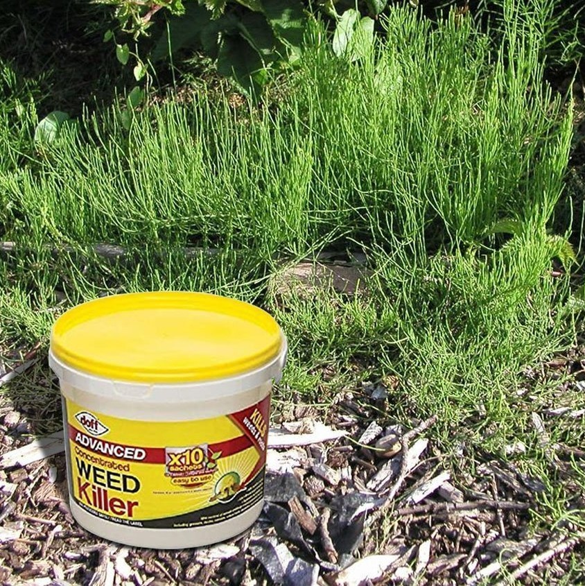Container of Doff Advanced Weed and Root Killer placed on garden mulch with green plants in the background.