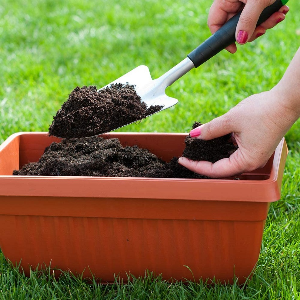 A person using a trowel to scoop peat-free compost into a terracotta planter on grass.