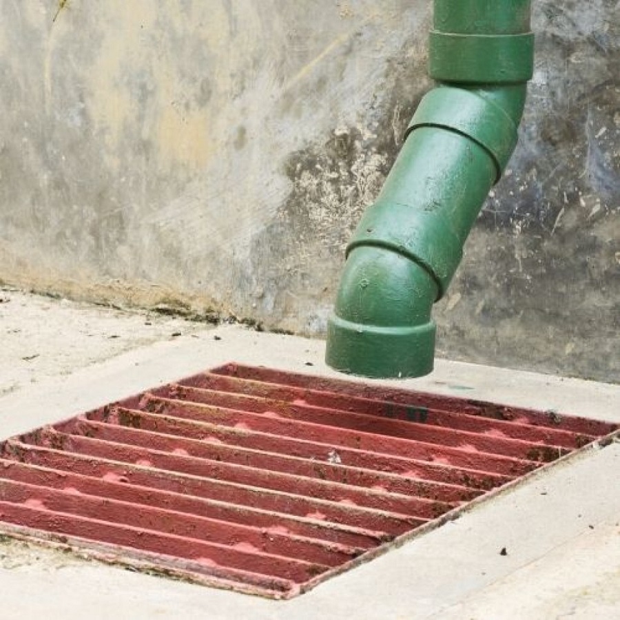 Green pipe leading into an outdoor drain with a red grate