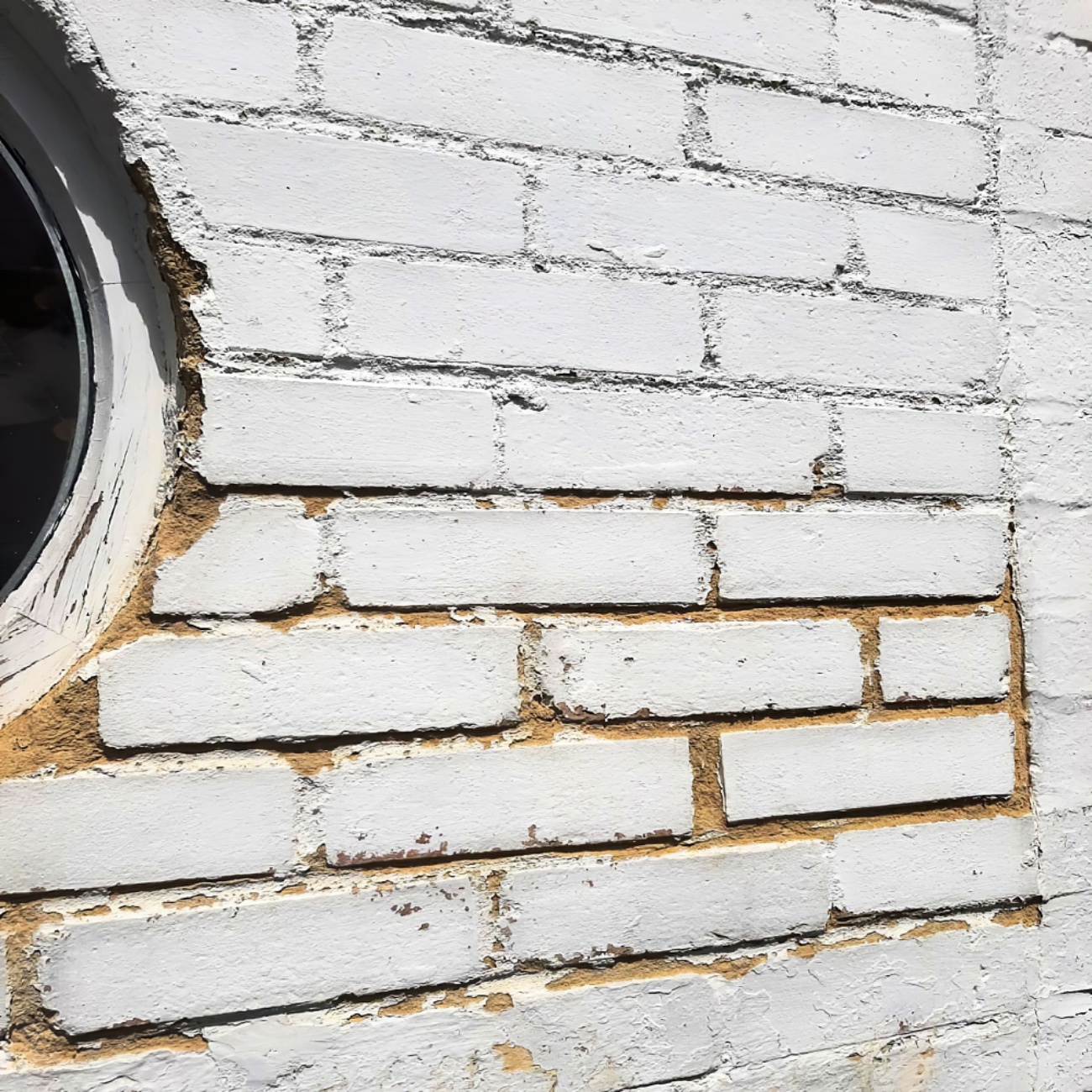 Everbuild 406 Close-up of a white painted brick wall with visible mortar lines and a round window edge.