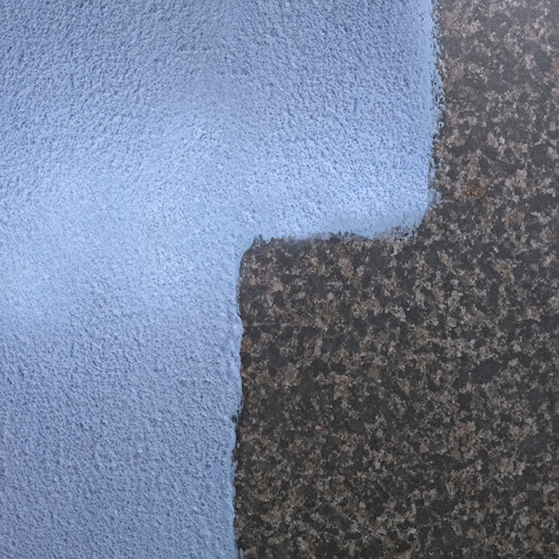 Close-up of a blue textured plaster coat applied on a dark surface.