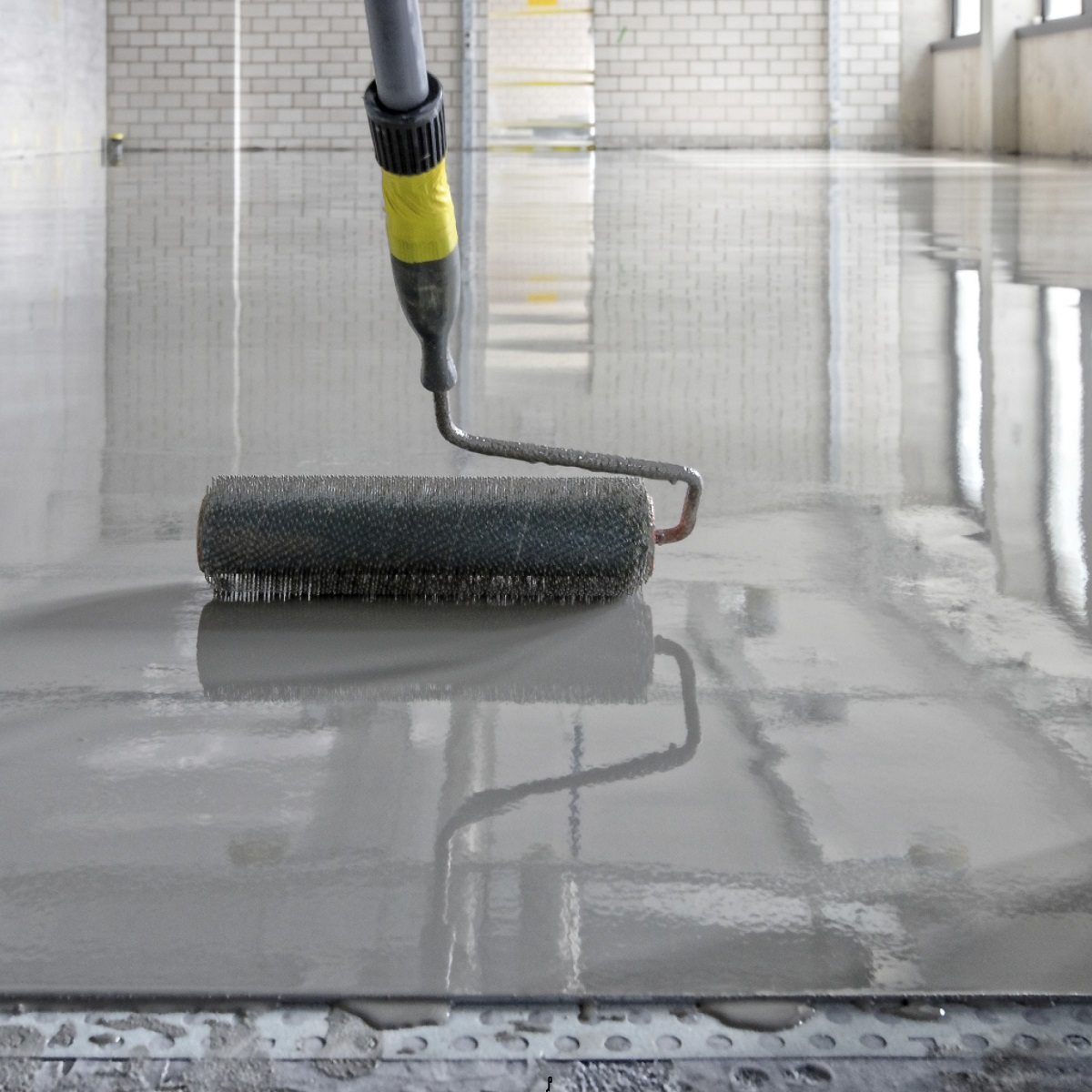 A roller applying a smooth layer of liquid on a concrete floor.