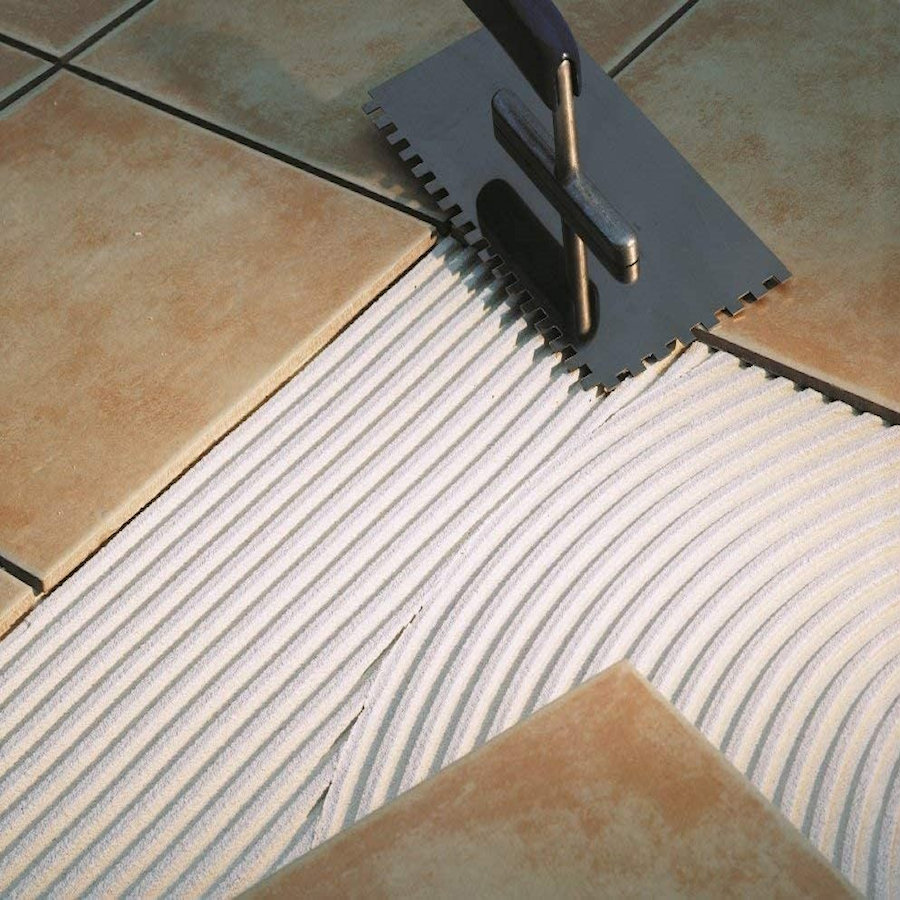 Trowel spreading adhesive on a floor with tiles being laid.