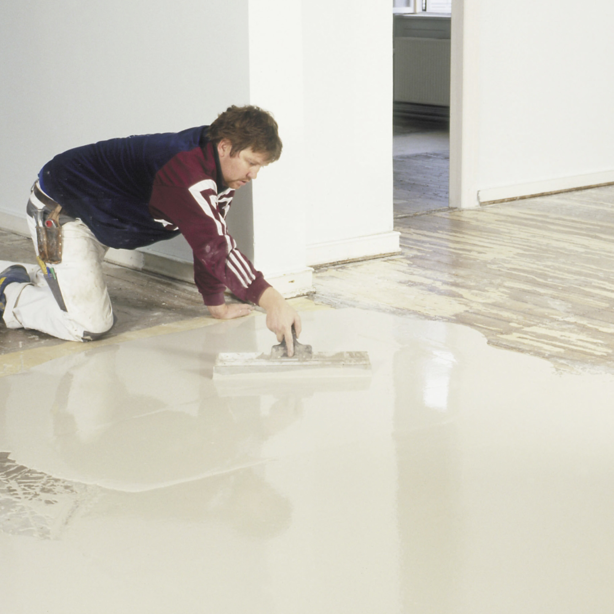 Person applying floor levelling compound with a trowel in a room.