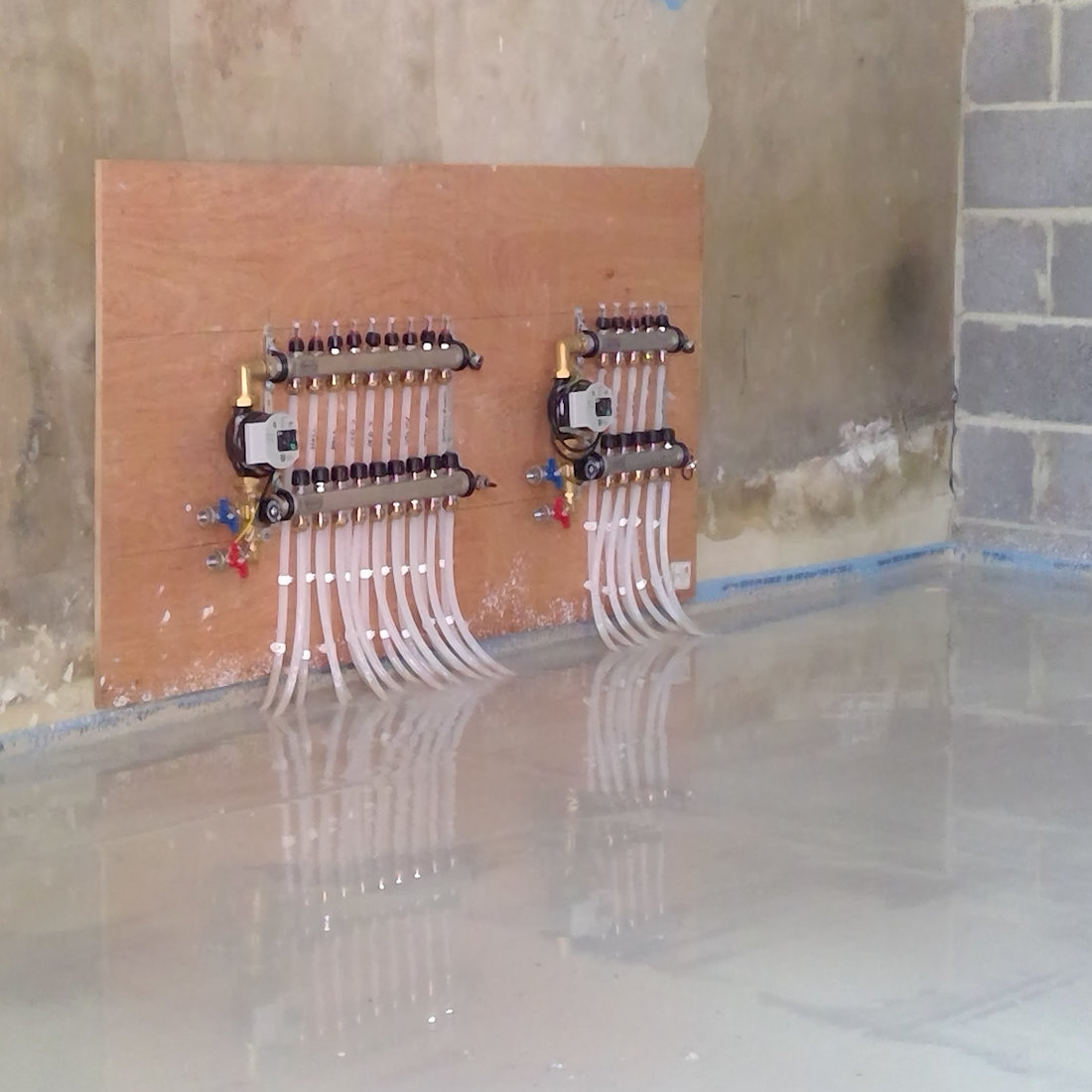 A freshly levelled floor with visible underfloor heating pipes and manifolds.