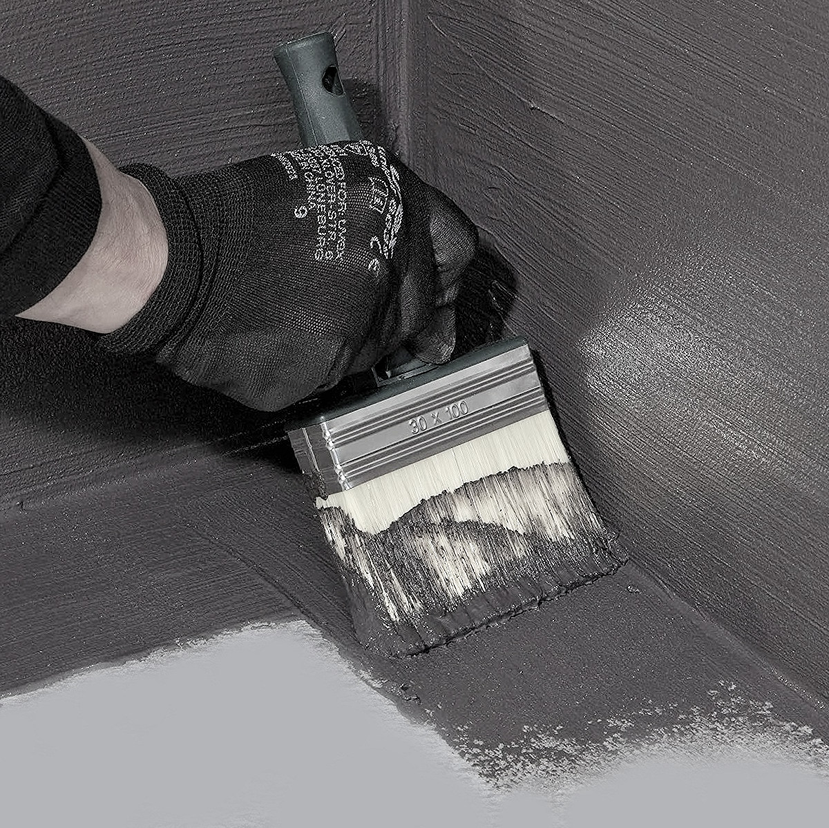A person applying Everbuild 908 Damp Proof Liquid Membrane with a brush to a surface.