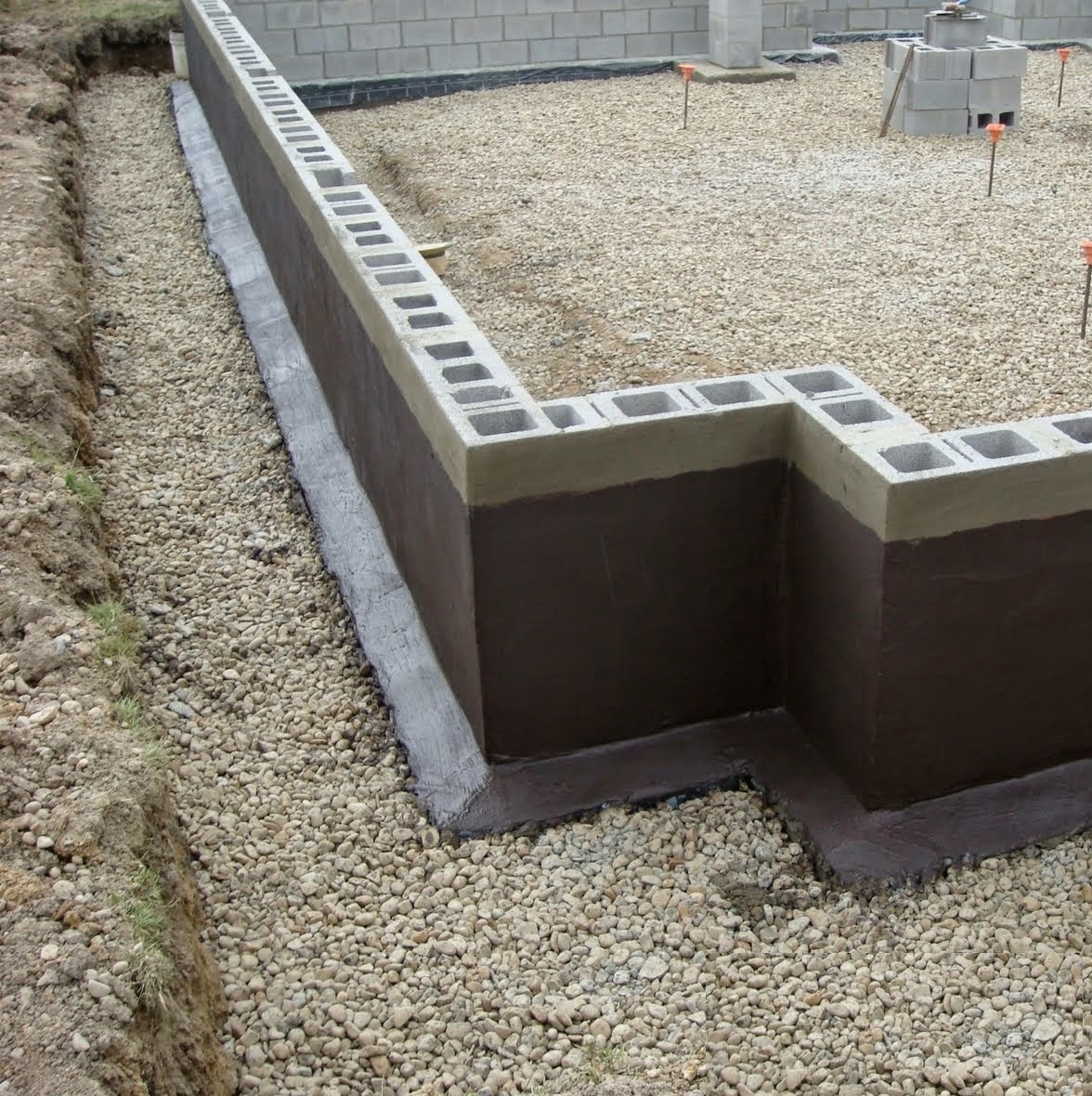 Foundation wall coated with a damp proof membrane, surrounded by gravel.