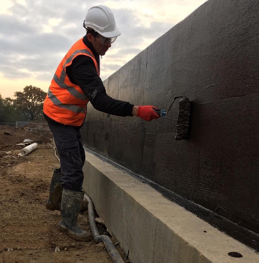 Worker applying damp proof membrane to a wall with a roller.