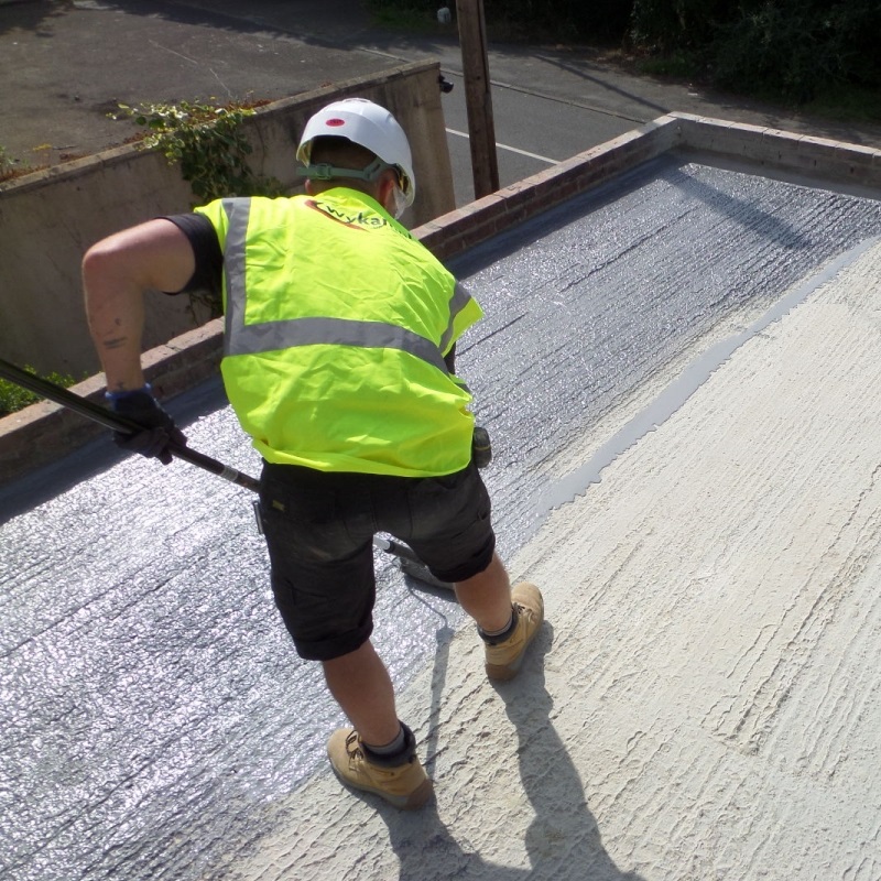 Worker applying a liquid membrane on a flat roof surface.