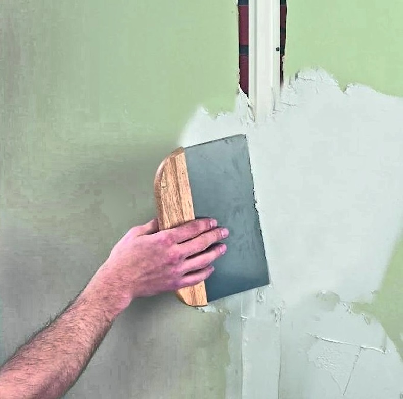 Hand applying plaster to a wall using a trowel.