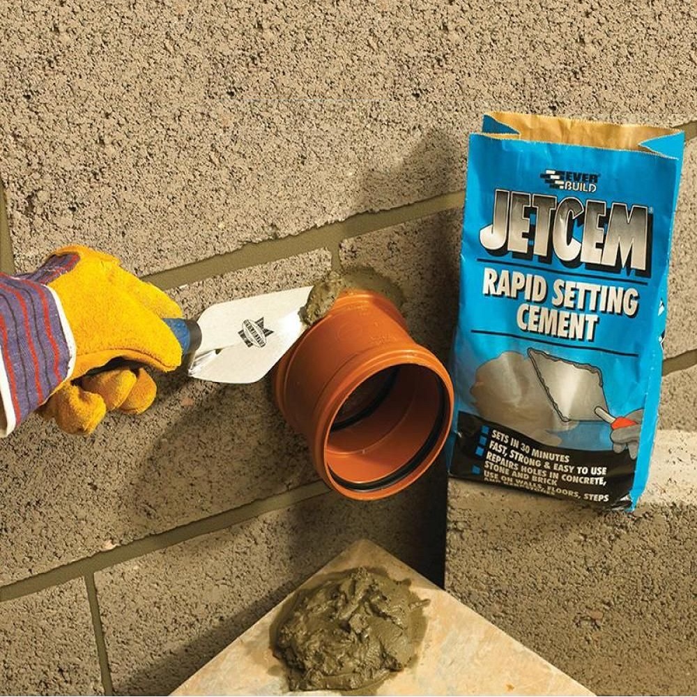 Person applying Everbuild Jetcem Rapid Setting Cement to a wall with a trowel, next to a bag of the product.