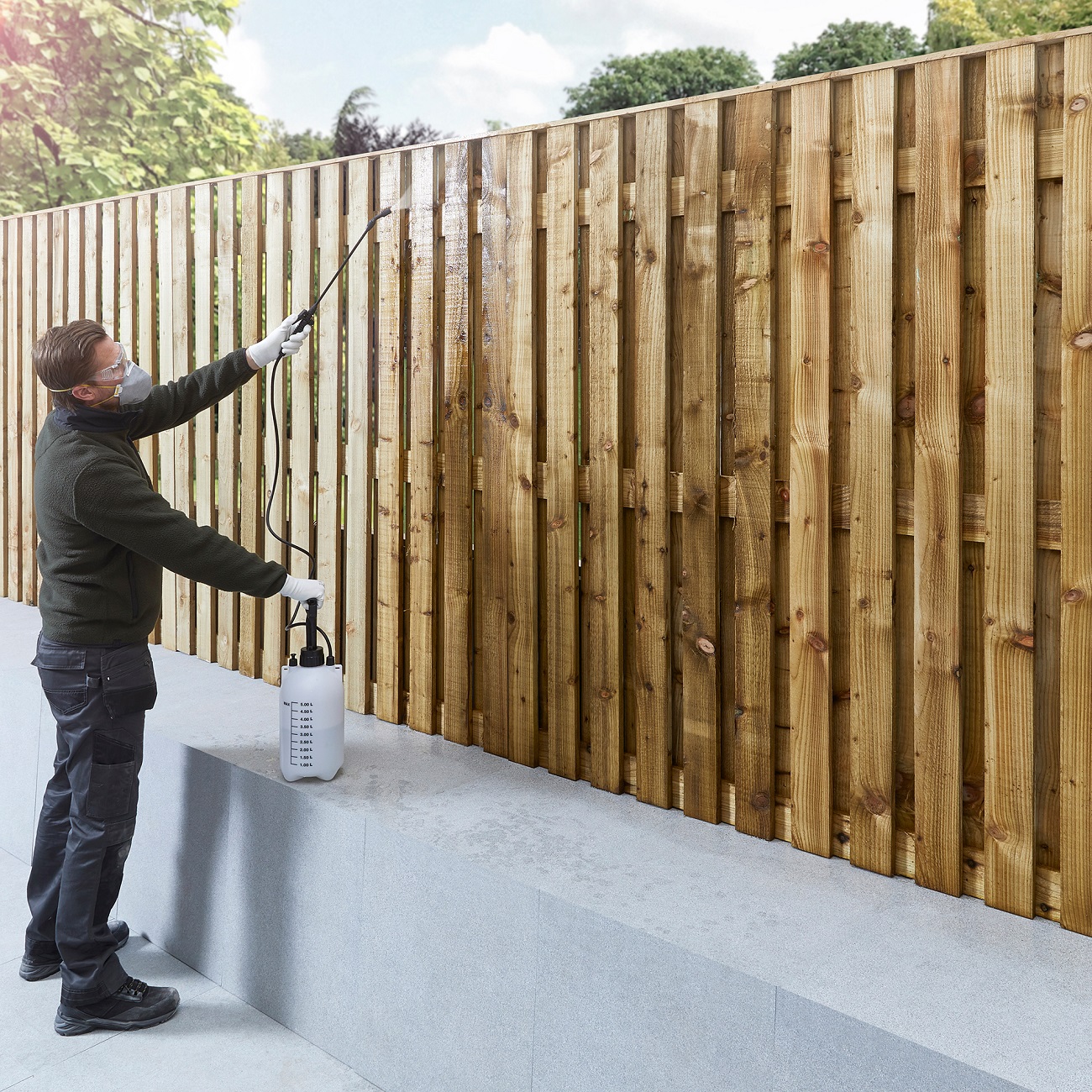 Person applying wood preserver to a wooden fence using a spray bottle.
