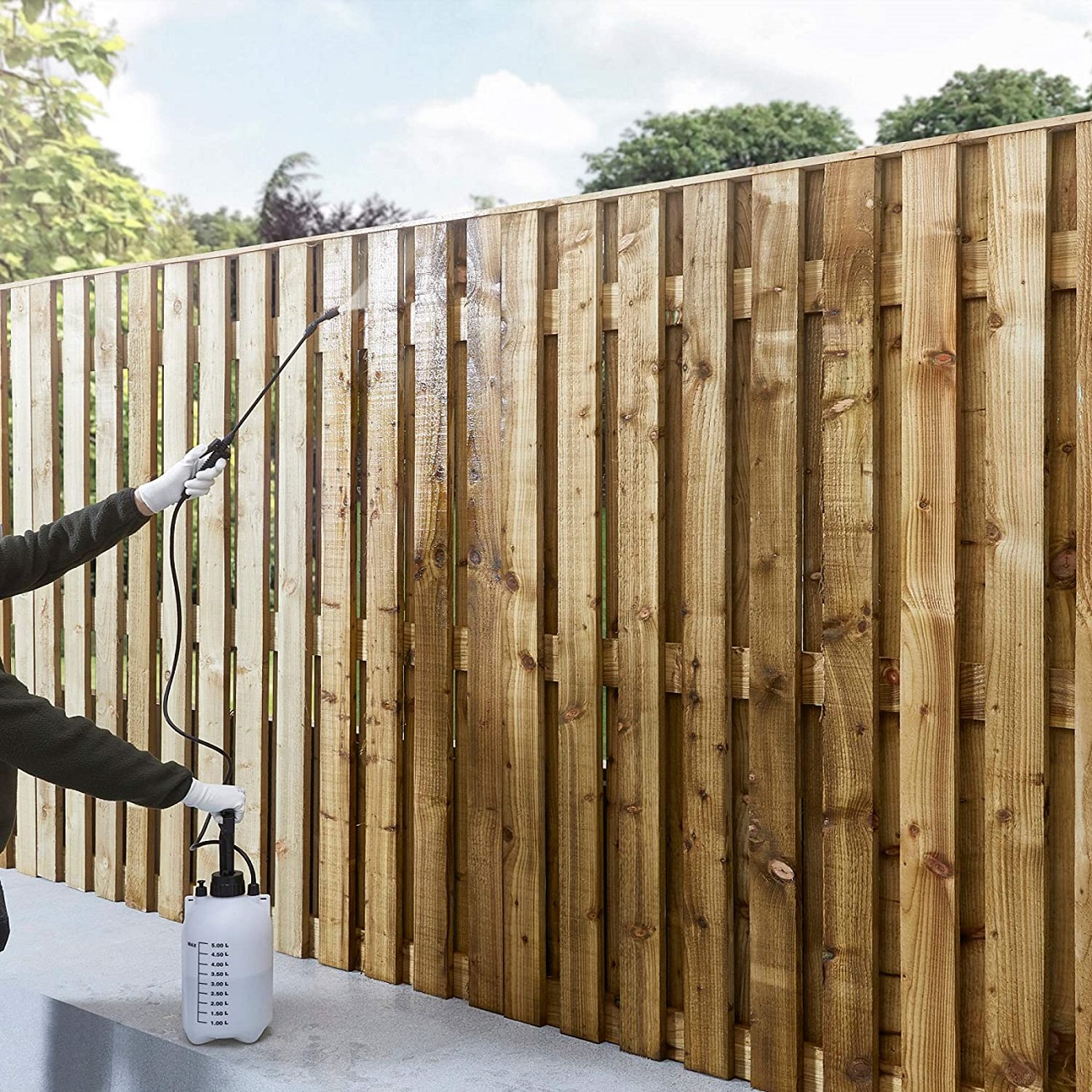 Person applying wood preserver to a wooden fence using a spray bottle.