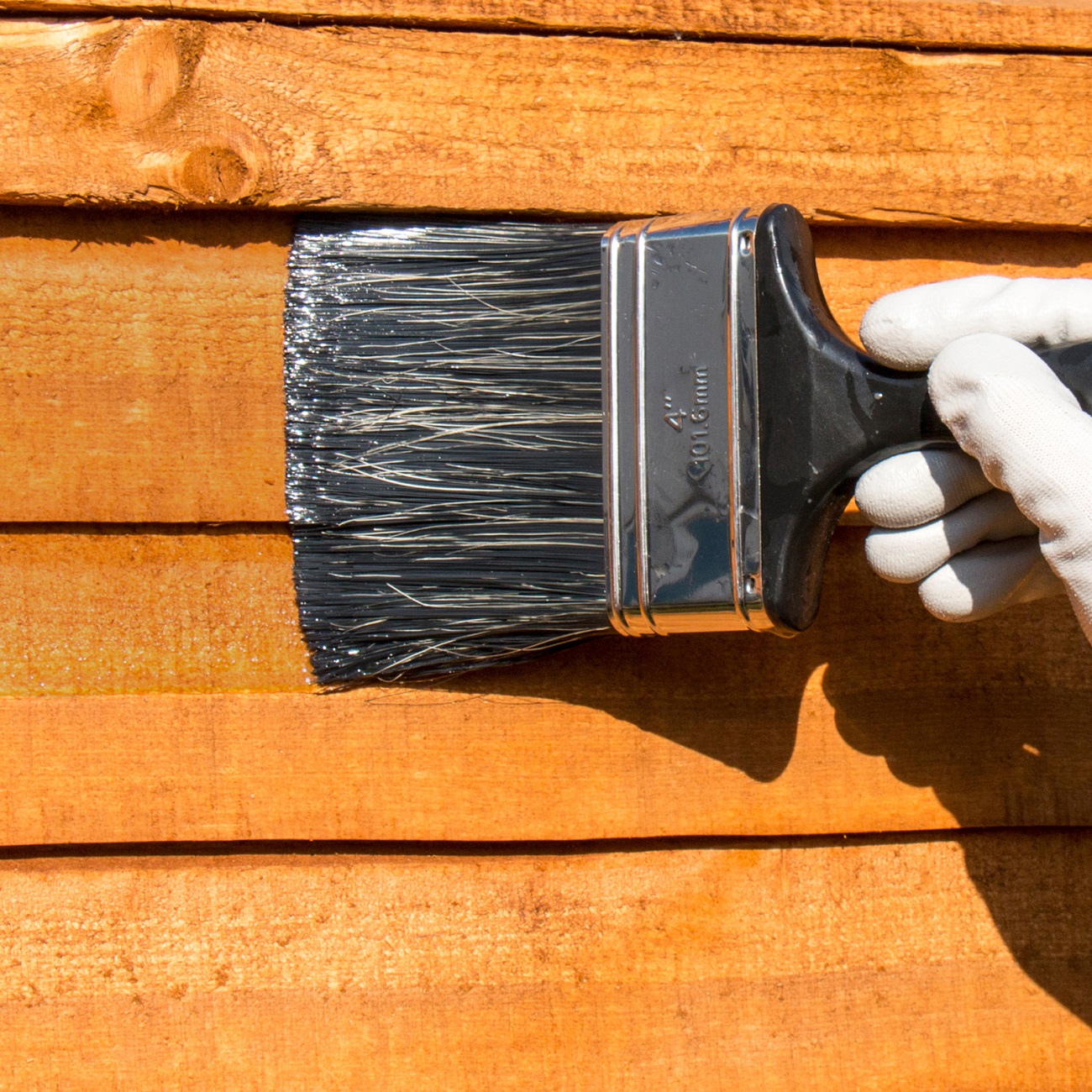 A person applying clear wood preserver to wooden planks using a brush.
