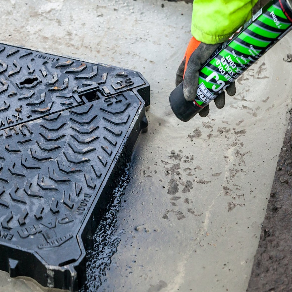 Person applying Bond It Instant Pot Hole Repair Tarmac around a manhole cover on a road surface.