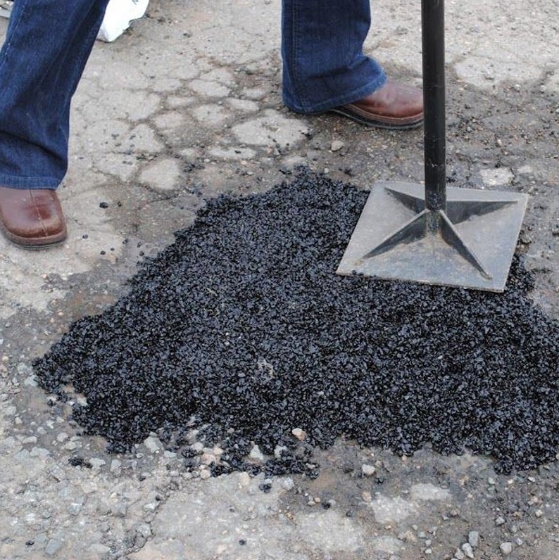 Person using a tamper to apply Bond It Instant Pot Hole Repair Tarmac on a road surface.