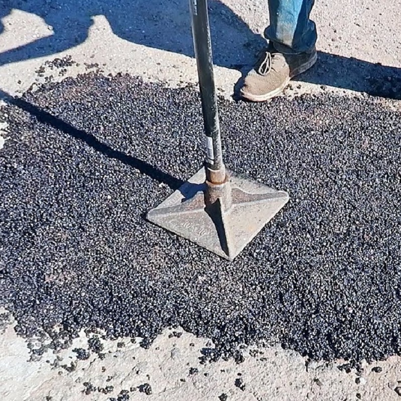 A person using a tamper tool to apply Bond It Instant Pot Hole Repair Tarmac on a road surface.