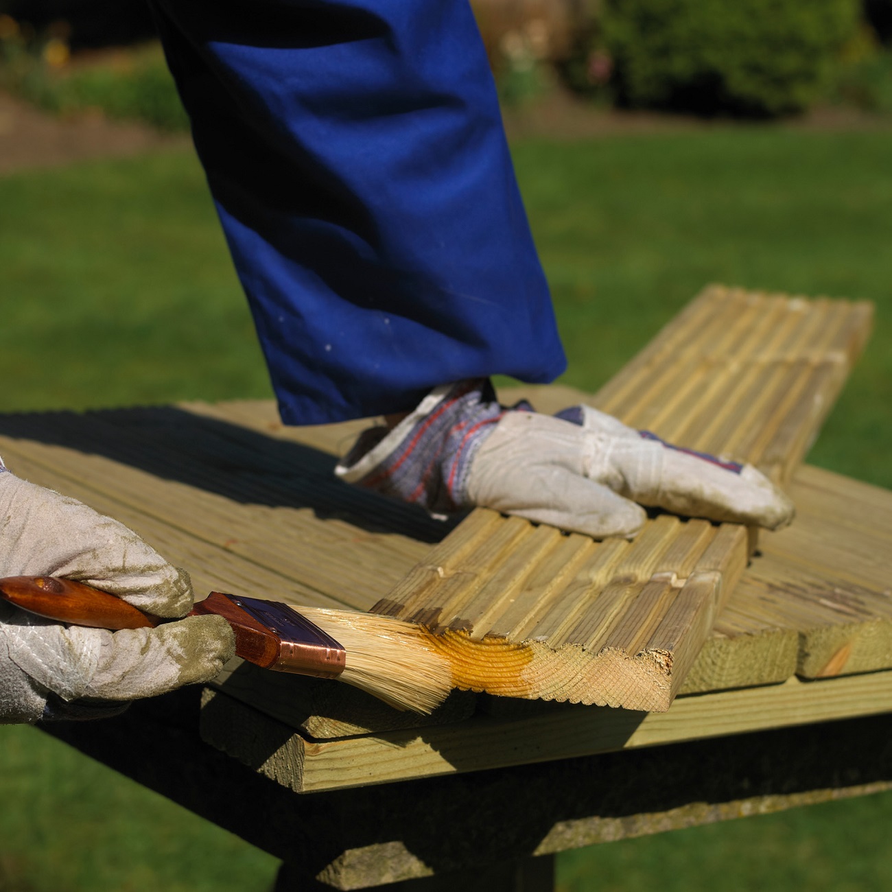 Person applying wood treatment with a brush on wooden planks outdoors.
