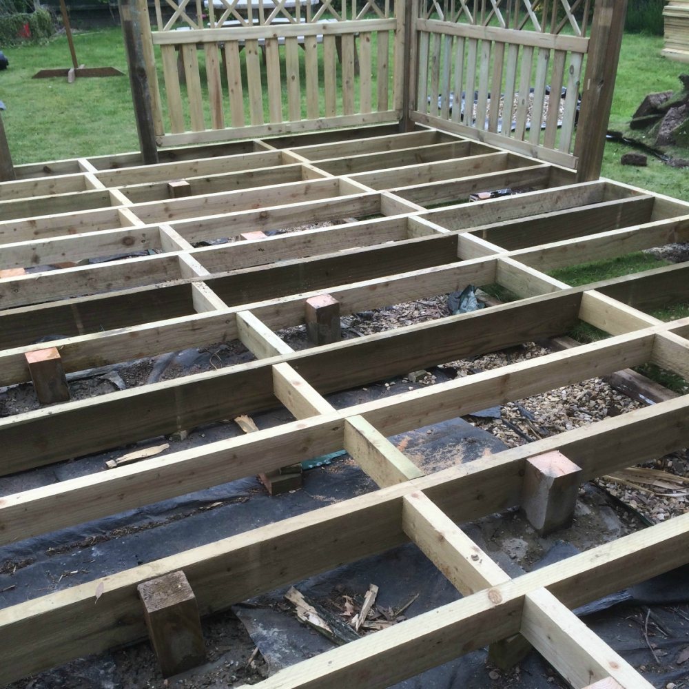 Wooden decking frame structure in a garden setting.