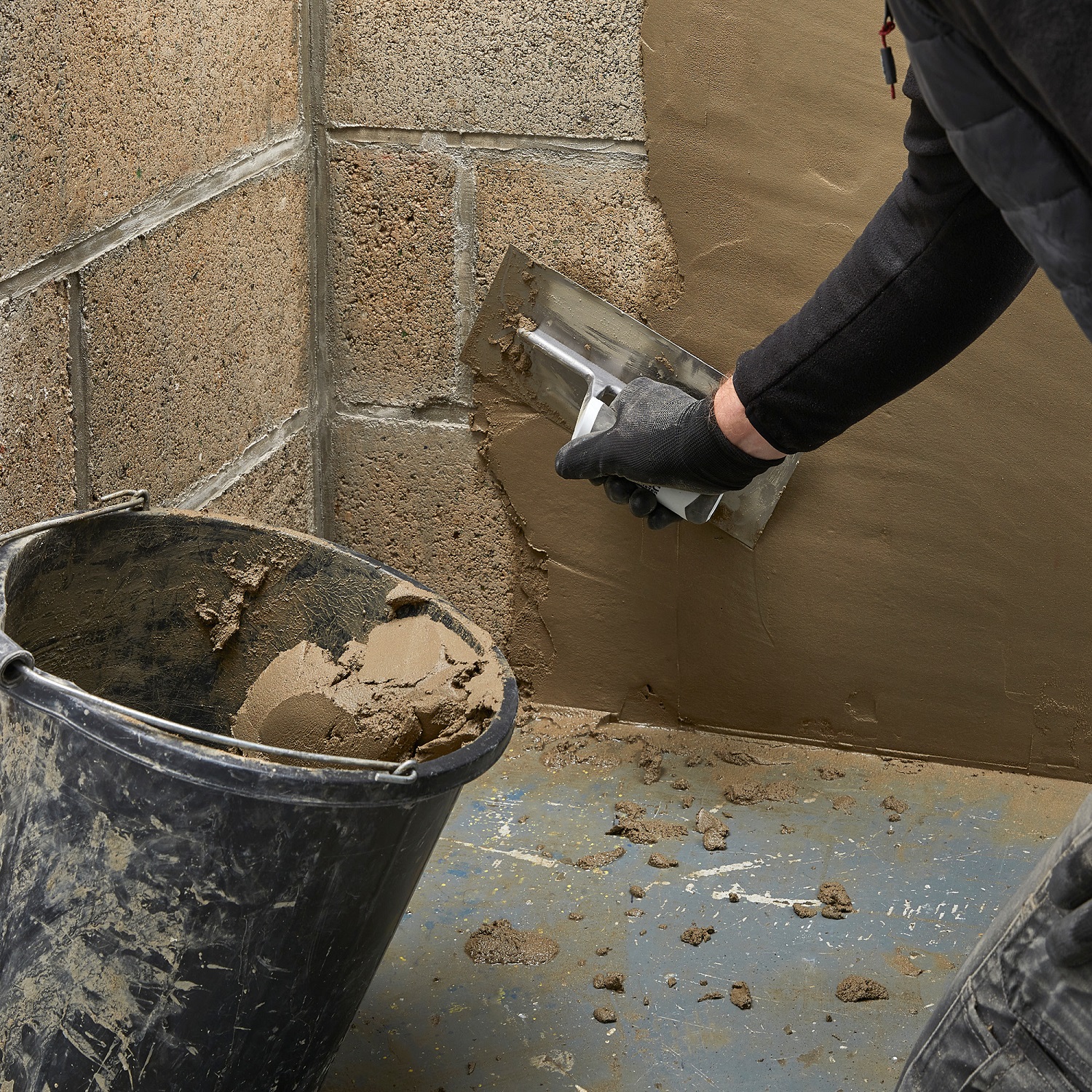 Person applying water stop repair compound to a wall using a trowel, with a bucket of mixed compound nearby.