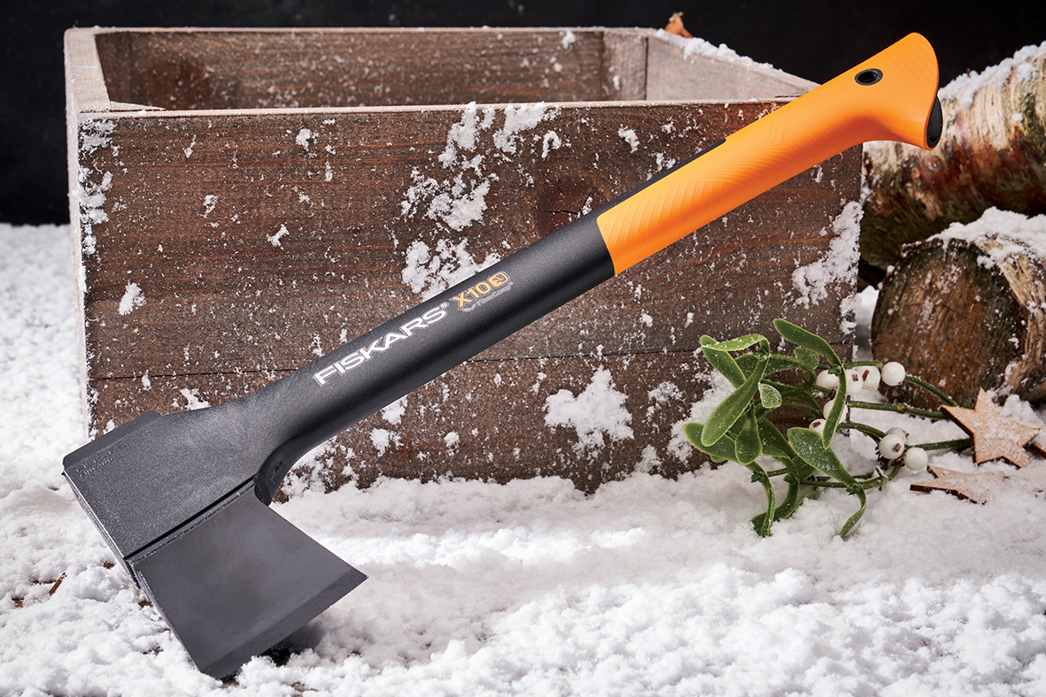 Fiskars axe with orange handle resting on snow-covered ground beside a wooden box and logs.