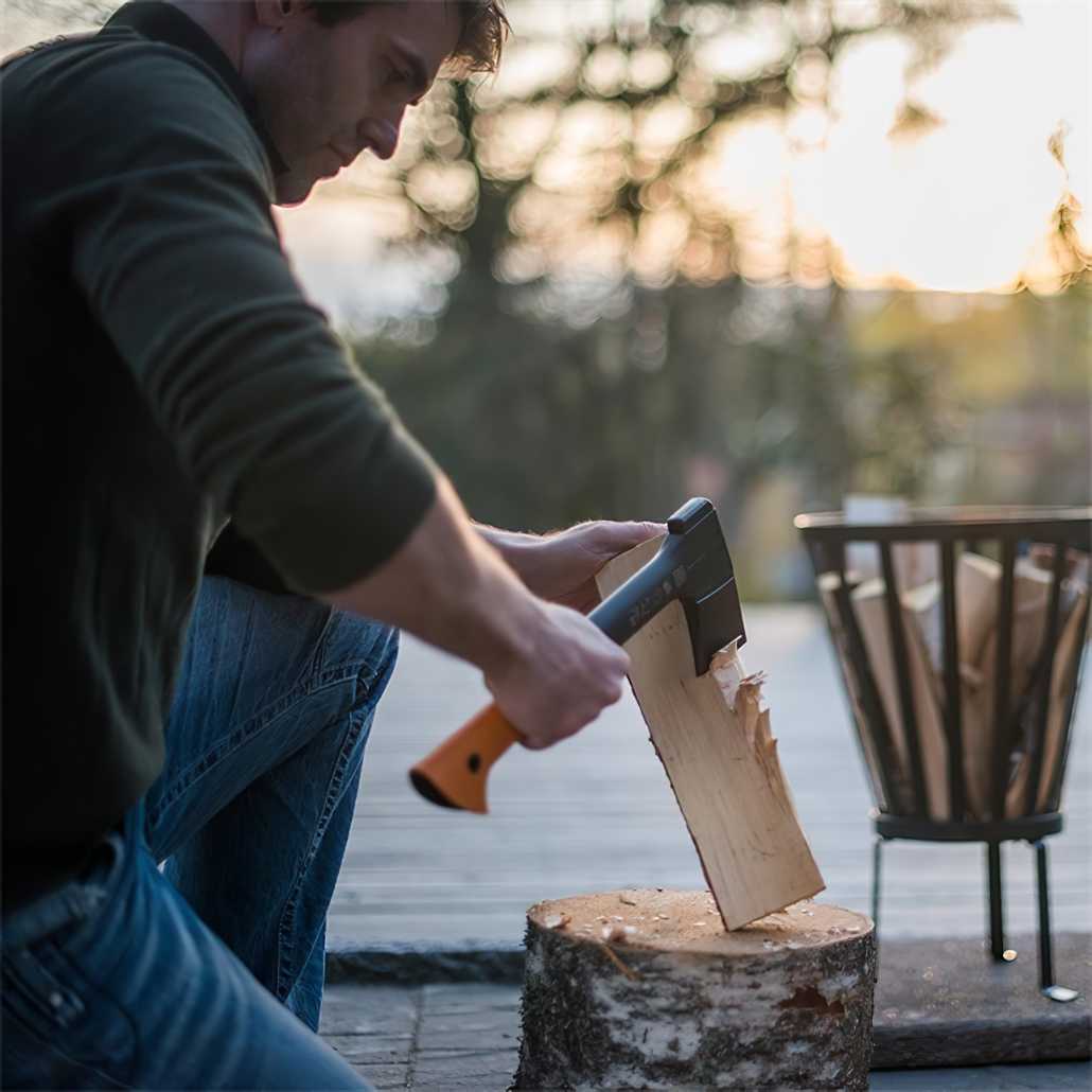 Person using a Fiskars axe to chop wood on a tree stump outdoors.