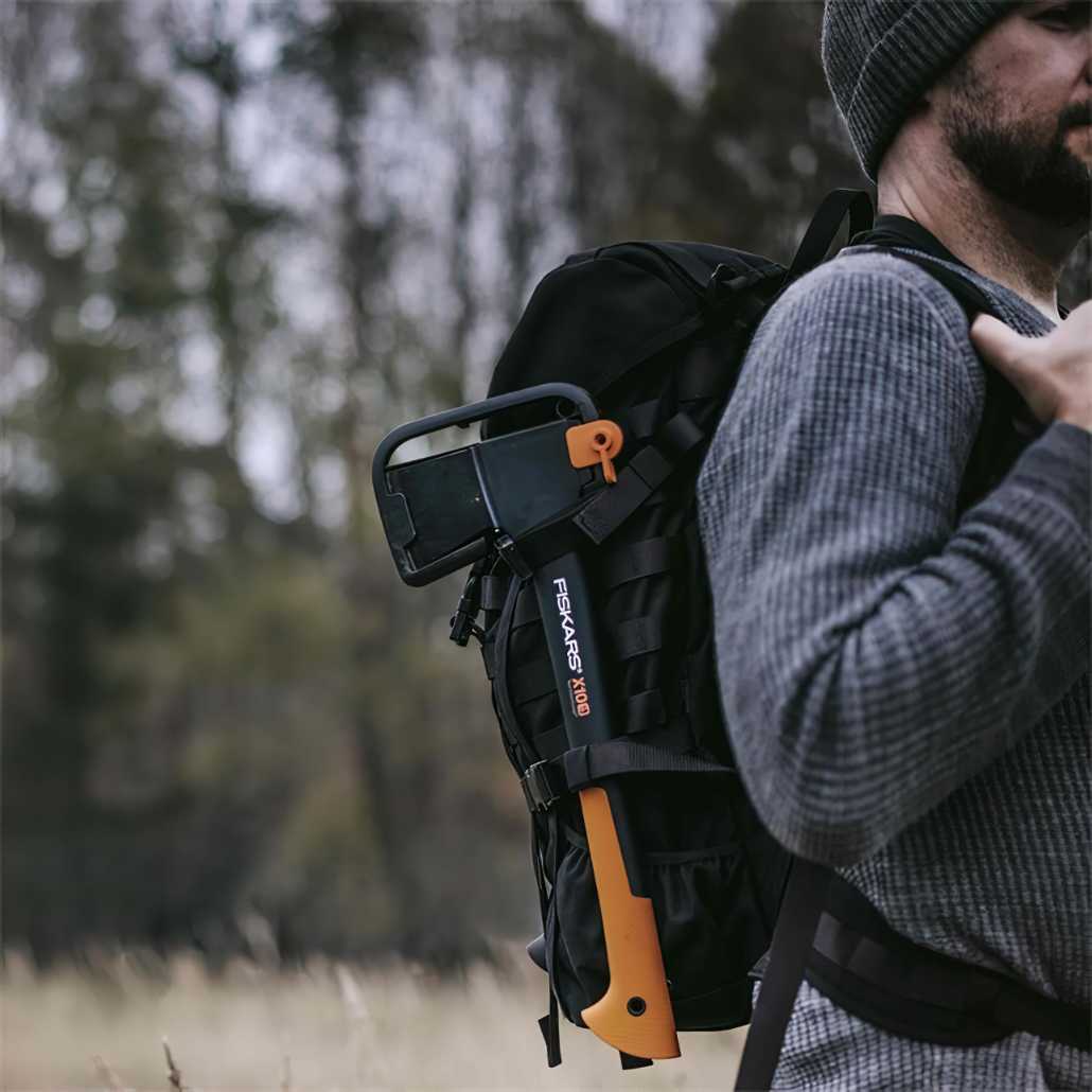 Person carrying a backpack with a Fiskars Premium Multi-Purpose Chopping Axe S attached, in an outdoor setting.