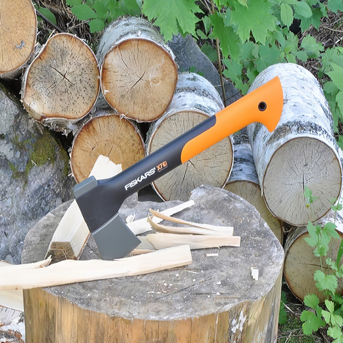 Fiskars axe with orange handle on a wooden stump surrounded by chopped logs.