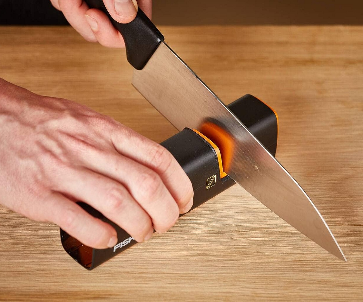 Fiskars knife sharpener with black and orange design sharpening a large kitchen knife