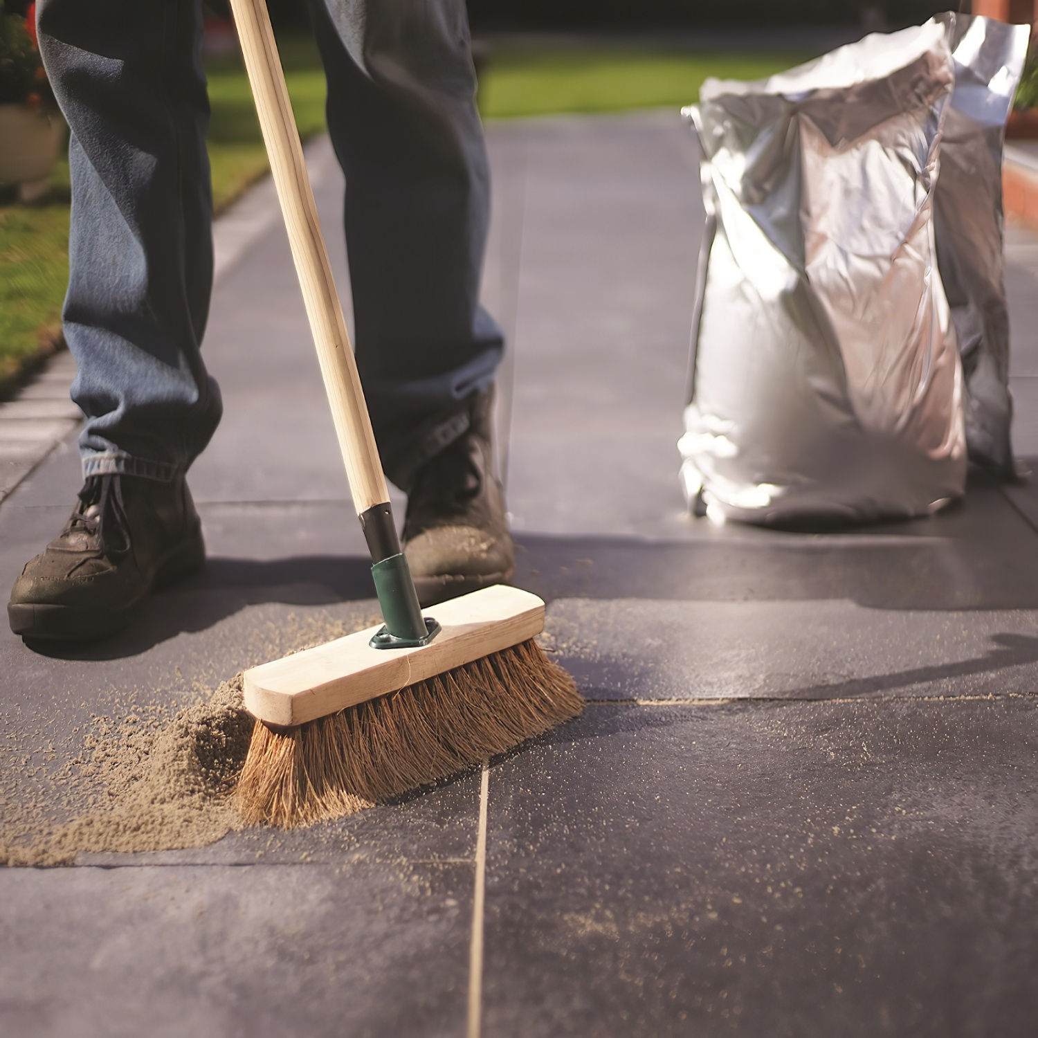 Person sweeping Geo-Fix compound into joints between slate paving slabs using a soft broom