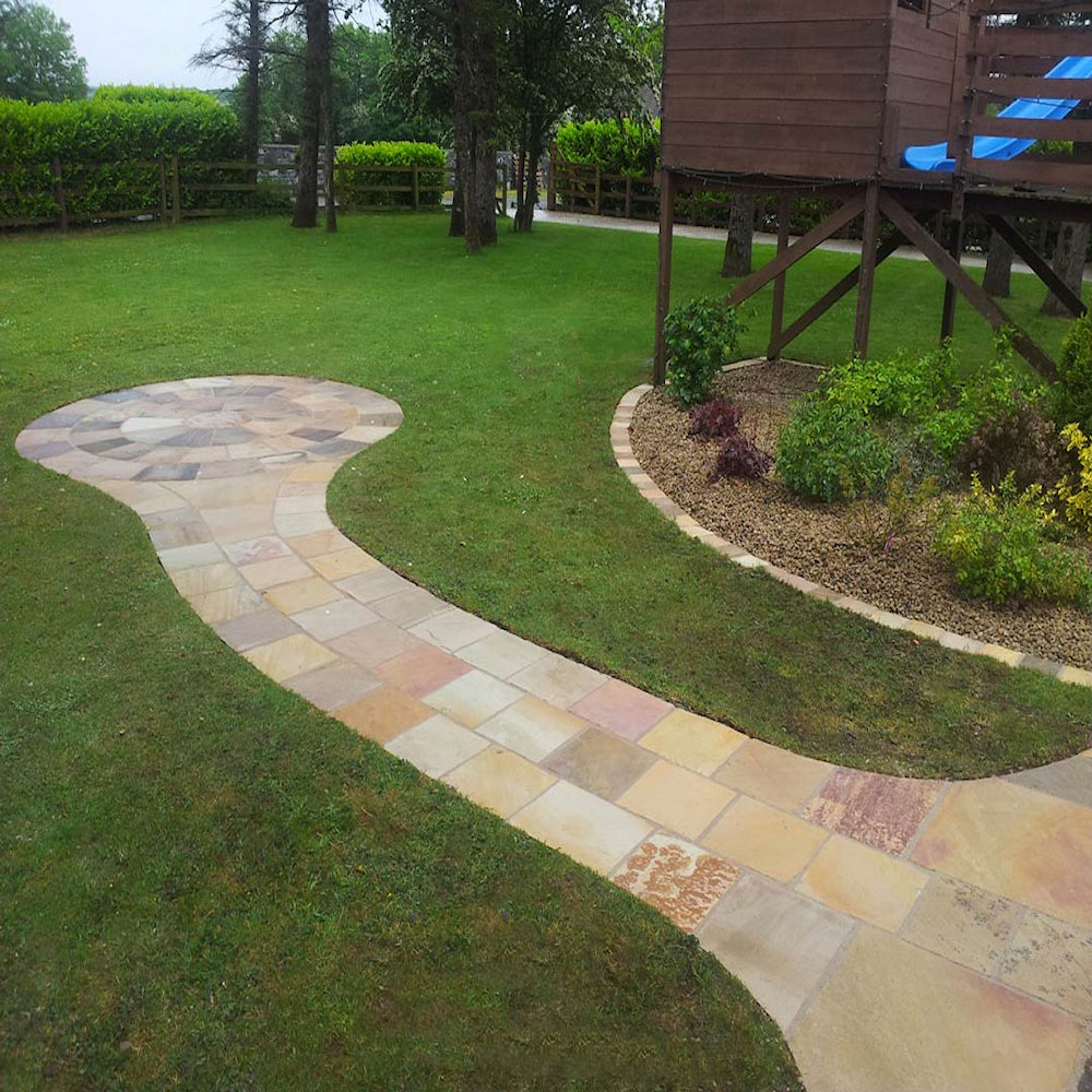 A garden path made of stone slabs, surrounded by grass and a wooden play structure.